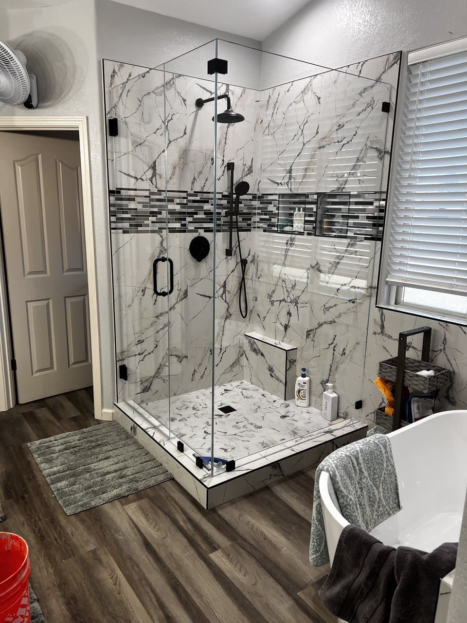 Marble shower with glass enclosure and mosaic accent by Russell Tile